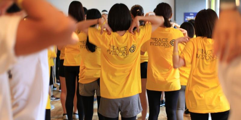 Group of L'OCCITANE employees with a yellow t-shirt with the Race for Vision Logo doing warm-ups before racing